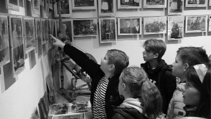 Eine Gruppe von Kinder beim Betrachten von Fotografien, die an einer Wand hängen.